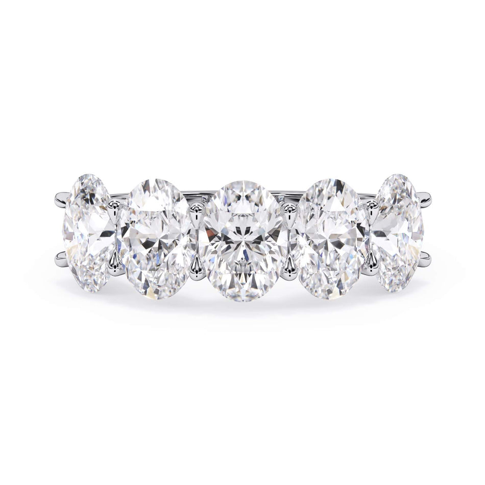 A picture of a five stone diamond wedding ring with oval shape diamonds that are u prong set in white gold or platinum on a white background with the ring facing forward, lying down.
