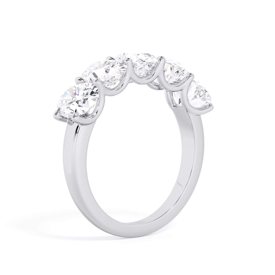 A picture of a five stone diamond wedding ring with oval shape diamonds that are u prong set in white gold or platinum on a white background with a slightly angled, through the finger view.