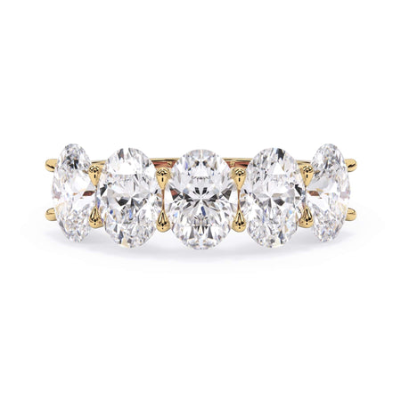 A picture of a five stone diamond wedding ring with oval shape diamonds that are u prong set in yellow gold on a white background with the ring facing forward, lying down.