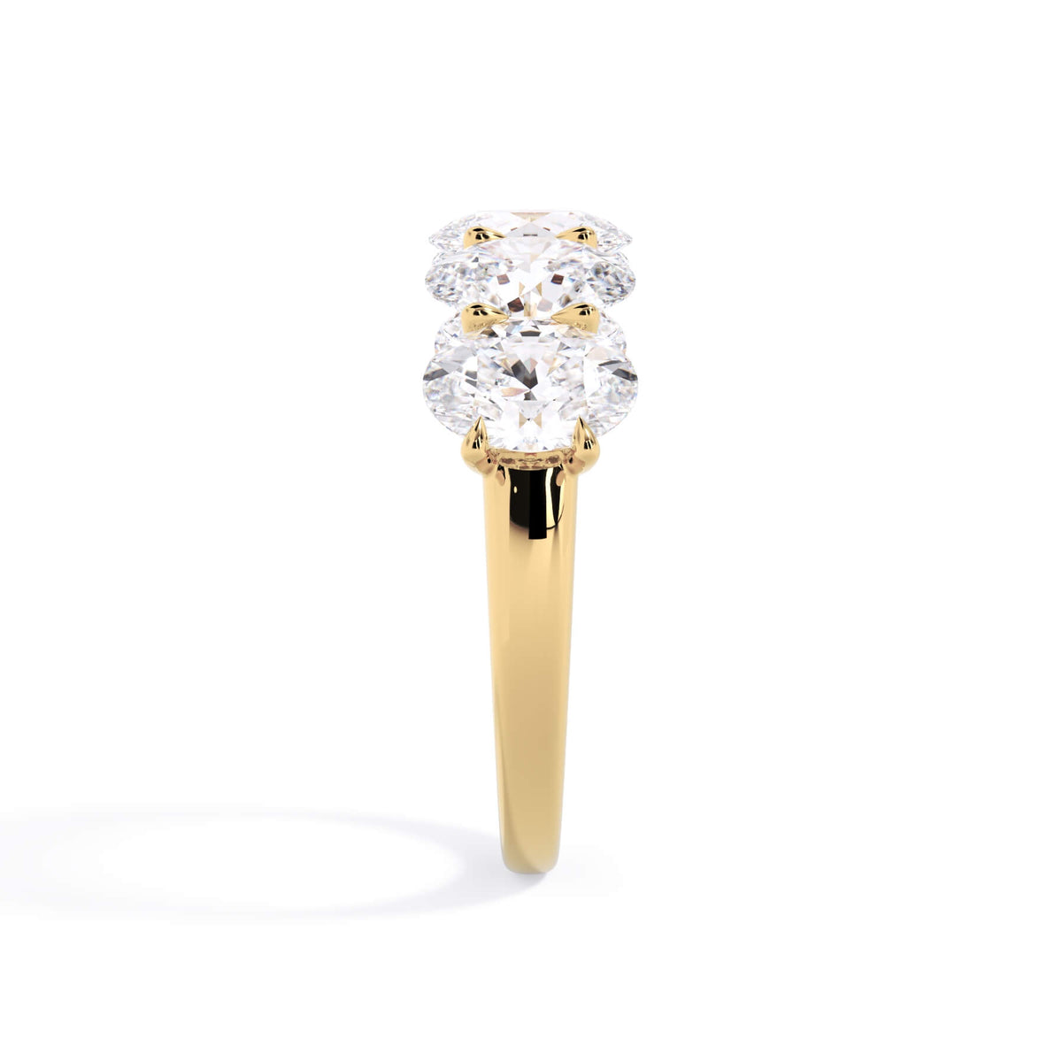 A picture of a five stone diamond wedding ring with oval shape diamonds that are u prong set in yellow gold on a white background with a side profile view.