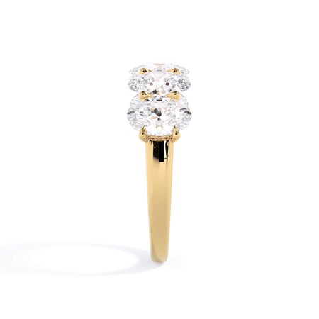 A picture of a five stone diamond wedding ring with oval shape diamonds that are u prong set in yellow gold on a white background with a side profile view.