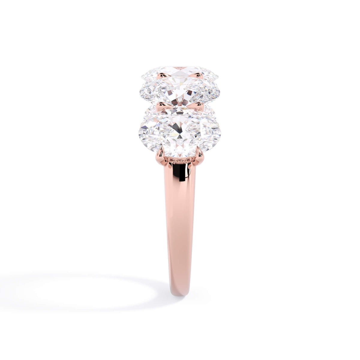 A picture of a five stone diamond wedding ring with oval shape diamonds that are u prong set in rose gold on a white background with a side profile view.