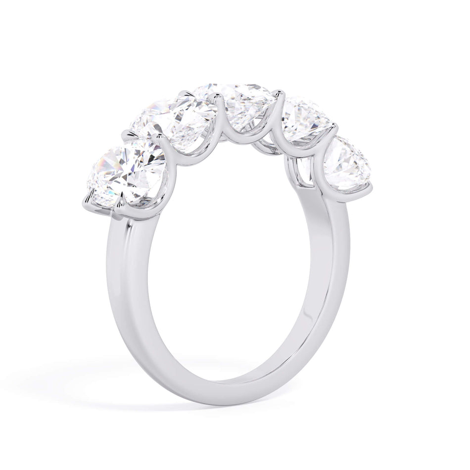 A picture of a five stone diamond wedding ring with oval shape diamonds that are u prong set in white gold or platinum on a white background with a slightly angled, through the finger view.