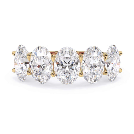 A picture of a five stone diamond wedding ring with oval shape diamonds that are u prong set in yellow gold on a white background with the ring facing forward, lying down.