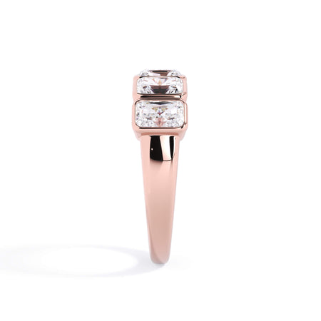 A picture of a five stone diamond wedding ring with radiant cut diamonds that are bezel set in rose gold on a white background with a side profile view.