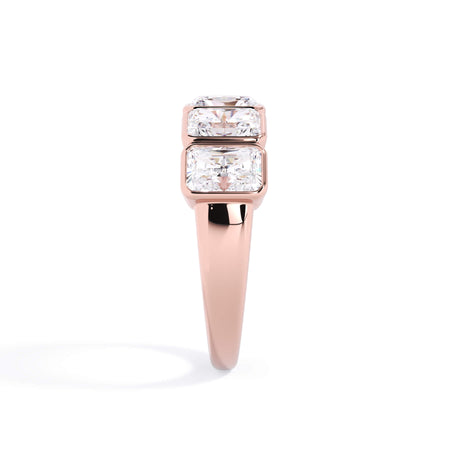 A picture of a five stone diamond wedding ring with radiant cut diamonds that are bezel set in rose gold on a white background with a side profile view.