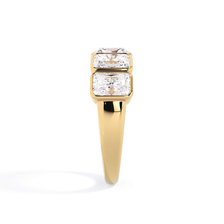 A picture of a five stone diamond wedding ring with radiant cut diamonds that are bezel set in yellow gold on a white background with a side profile view.