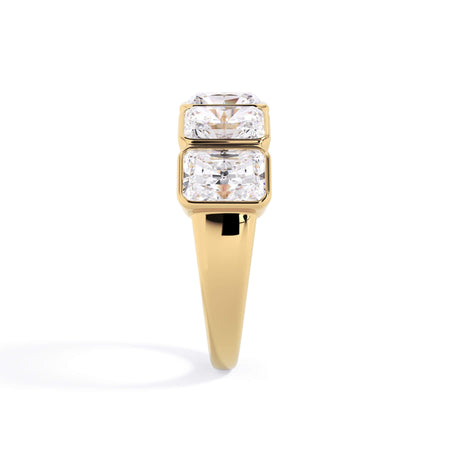 A picture of a five stone diamond wedding ring with radiant cut diamonds that are bezel set in yellow gold on a white background with a side profile view.