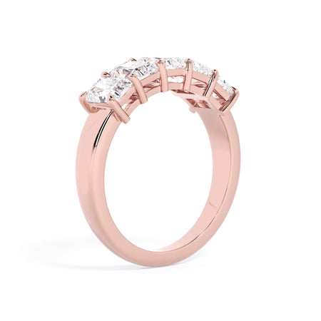 A picture of a five stone diamond wedding ring with radiant cut diamonds that are shared prong set in rose gold on a white background with a slightly angled, through the finger view.