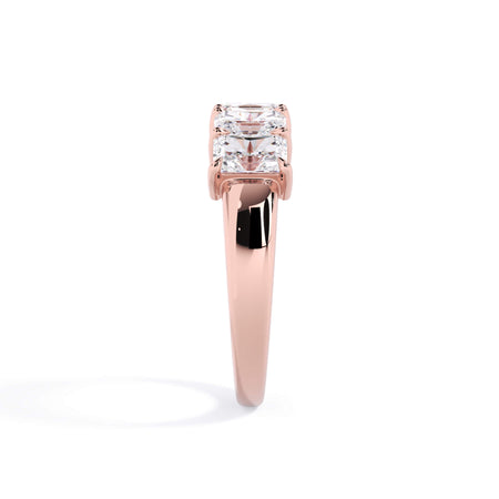 A picture of a five stone diamond wedding ring with radiant cut diamonds that are shared prong set in rose gold on a white background with a side profile view.