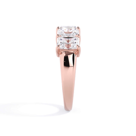 A picture of a five stone diamond wedding ring with radiant cut diamonds that are shared prong set in rose gold on a white background with a side profile view.