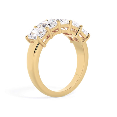 A picture of a five stone diamond wedding ring with radiant cut diamonds that are shared prong set in yellow gold on a white background with a slightly angled, through the finger view.