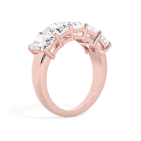 A picture of a five stone diamond wedding ring with radiant cut diamonds that are shared prong set in rose gold on a white background with a slightly angled, through the finger view.