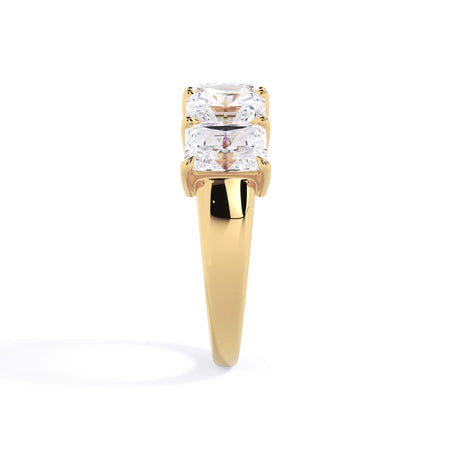 A picture of a five stone diamond wedding ring with radiant cut diamonds that are shared prong set in yellow gold on a white background with a side profile view.