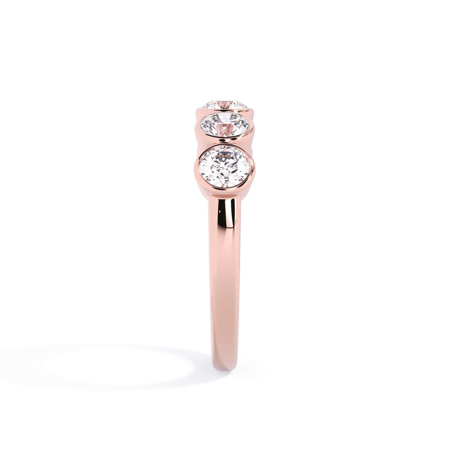 A picture of a five stone diamond wedding ring with round diamonds that are bezel set in rose gold on a white background with a side profile view.