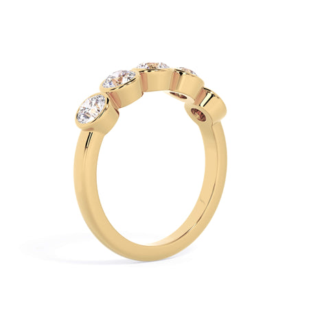 A picture of a five stone diamond wedding ring with round diamonds that are bezel set in yellow gold on a white background with a slightly angled, through the finger view.