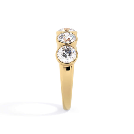 A picture of a five stone diamond wedding ring with round diamonds that are bezel set in yellow gold on a white background with a side profile view.
