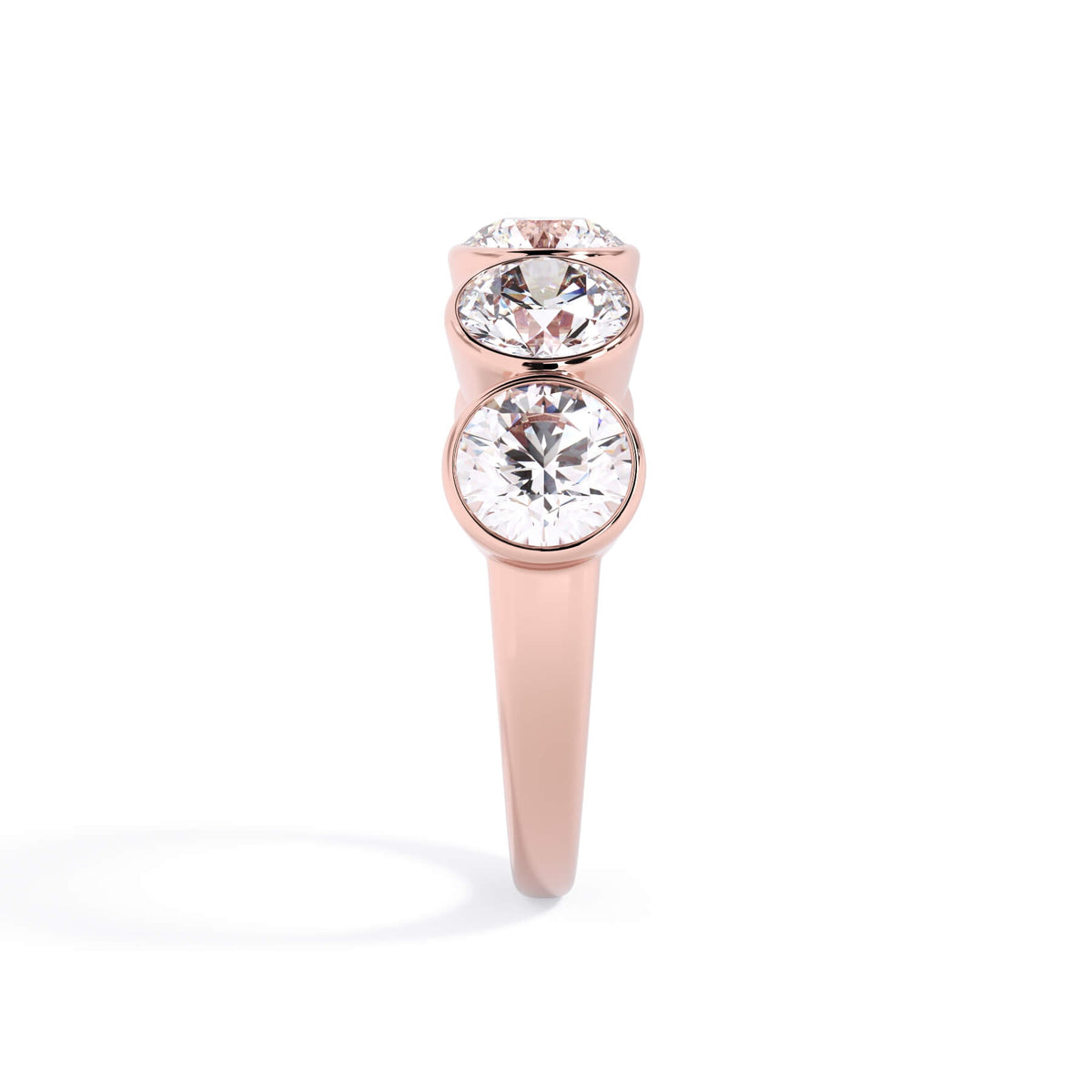 A picture of a five stone diamond wedding ring with round diamonds that are bezel set in rose gold on a white background with a side profile view.