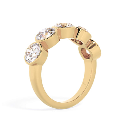 A picture of a five stone diamond wedding ring with round diamonds that are bezel set in yellow gold on a white background with a slightly angled, through the finger view.