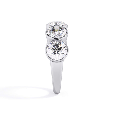 A picture of a five stone diamond wedding ring with round diamonds that are bezel set in white gold or platinum on a white background with a side profile view.