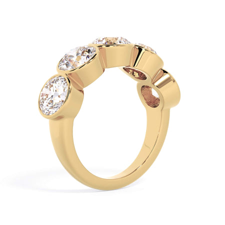 A picture of a five stone diamond wedding ring with round diamonds that are bezel set in yellow gold on a white background with a slightly angled, through the finger view.