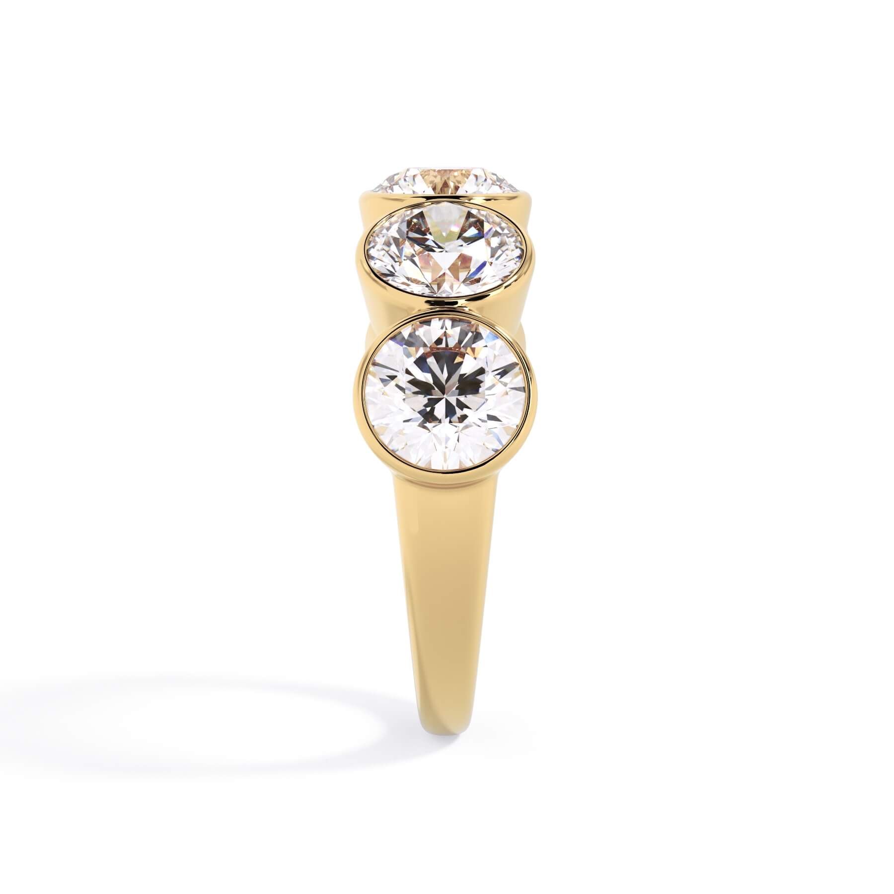 A picture of a five stone diamond wedding ring with round diamonds that are bezel set in yellow gold on a white background with a side profile view.