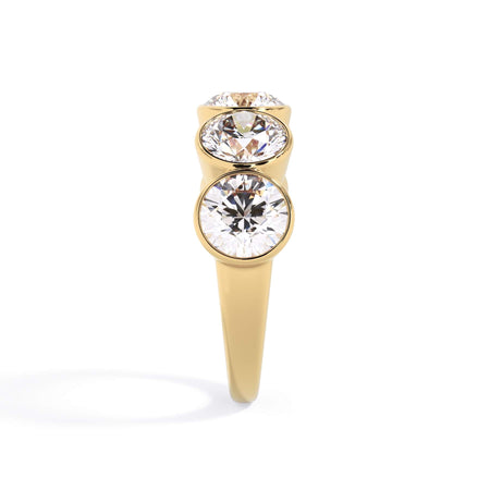 A picture of a five stone diamond wedding ring with round diamonds that are bezel set in yellow gold on a white background with a side profile view.