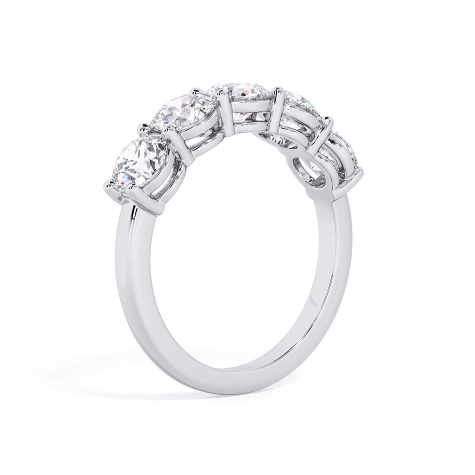 A picture of a five stone diamond wedding ring with round diamonds that are shared prong set in white gold or platinum on a white background with a slightly angled, through the finger view.