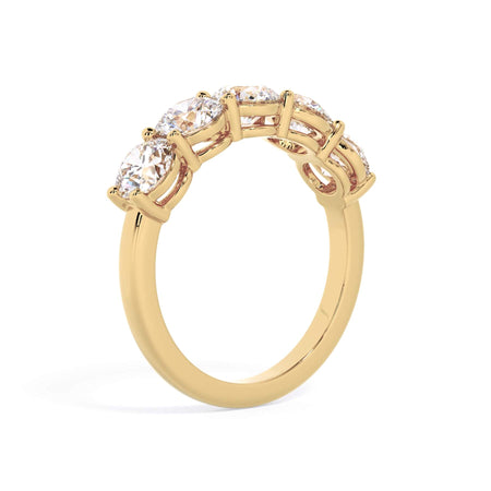 A picture of a five stone diamond wedding ring with round diamonds that are shared prong set in yellow gold on a white background with a slightly angled, through the finger view.