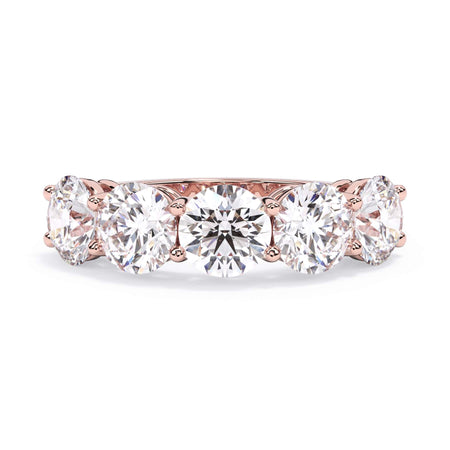 A picture of a five stone diamond wedding ring with round diamonds that are shared prong set in rose gold on a white background with the ring facing forward, lying down.