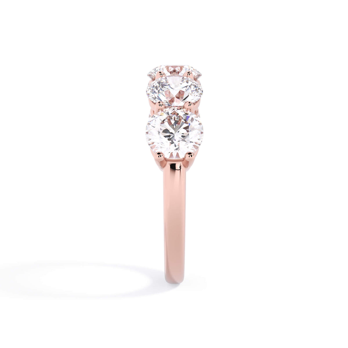 A picture of a five stone diamond wedding ring with round diamonds that are shared prong set in rose gold on a white background with a side profile view.