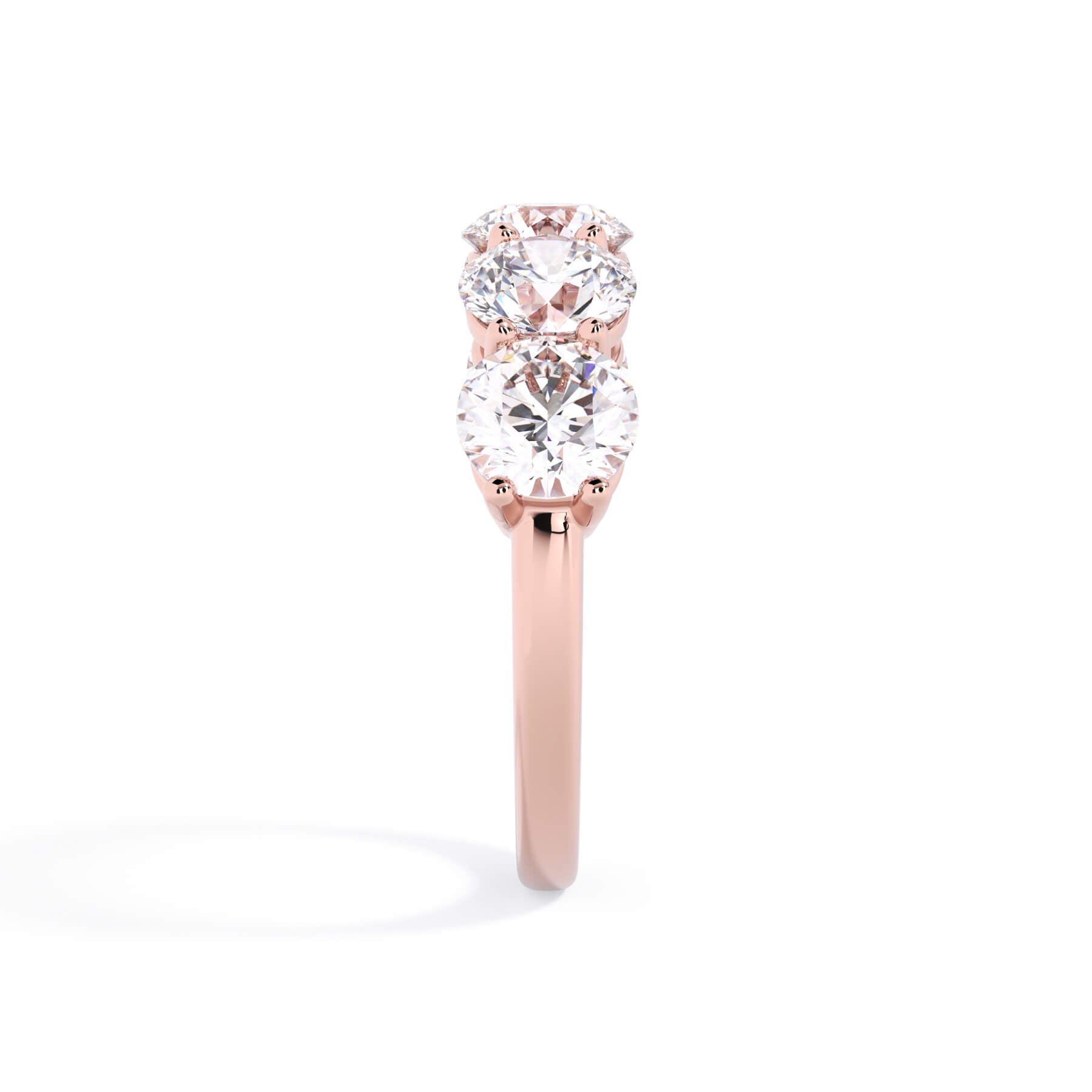 A picture of a five stone diamond wedding ring with round diamonds that are shared prong set in rose gold on a white background with a side profile view.