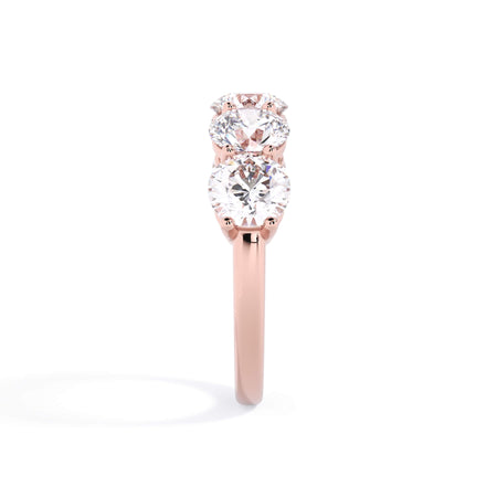 A picture of a five stone diamond wedding ring with round diamonds that are shared prong set in rose gold on a white background with a side profile view.