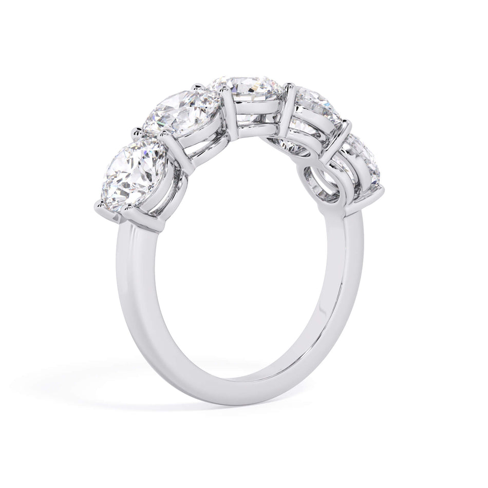 A picture of a five stone diamond wedding ring with round diamonds that are shared prong set in white gold or platinum on a white background with a slightly angled, through the finger view.