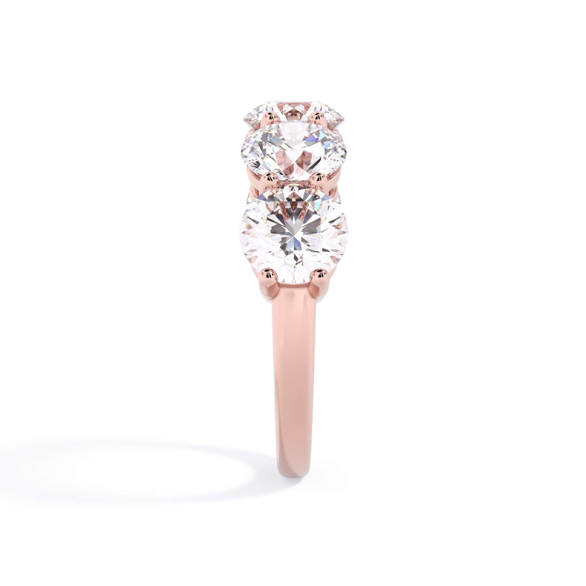 A picture of a five stone diamond wedding ring with round diamonds that are shared prong set in rose gold on a white background with a side profile view.