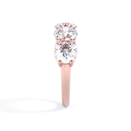 A picture of a five stone diamond wedding ring with round diamonds that are shared prong set in rose gold on a white background with a side profile view.