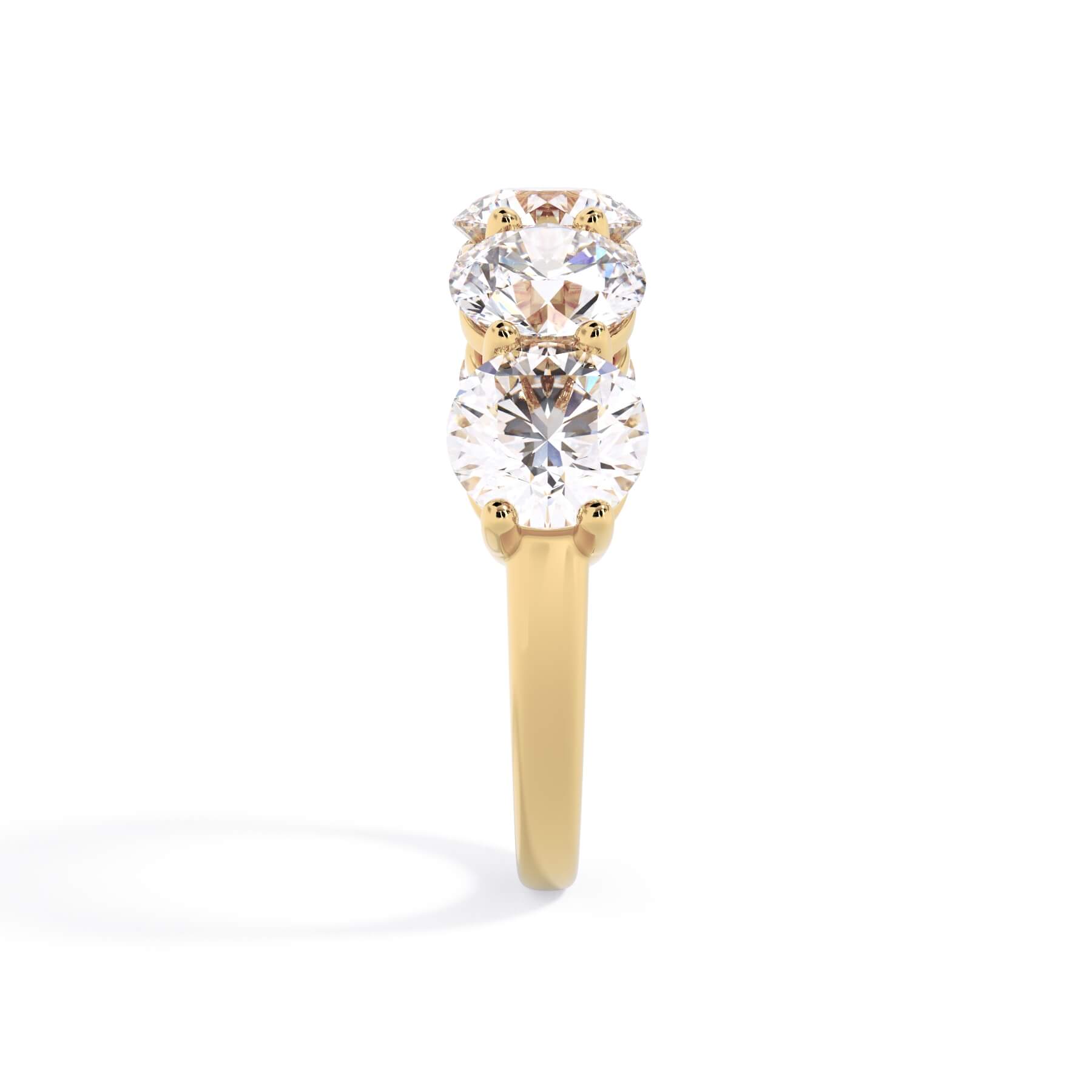 A picture of a five stone diamond wedding ring with round diamonds that are shared prong set in yellow gold on a white background with a side profile view.