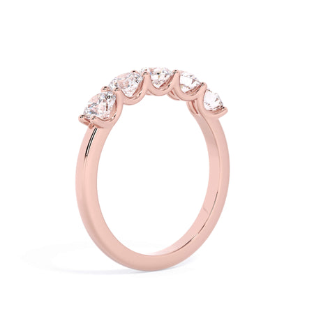A picture of a five stone diamond wedding ring with round diamonds that are u prong set in rose gold on a white background with a slightly angled, through the finger view.