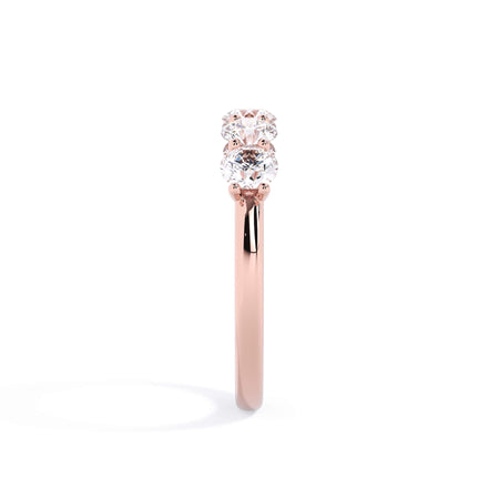 A picture of a five stone diamond wedding ring with round diamonds that are u prong set in rose gold on a white background with a side profile view.