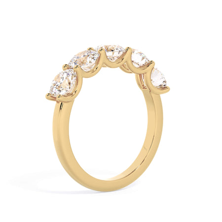 A picture of a five stone diamond wedding ring with round diamonds that are u prong set in yellow gold on a white background with a slightly angled, through the finger view.