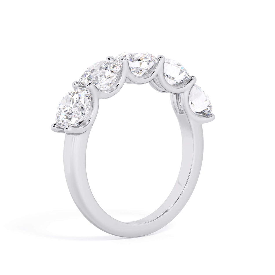 A picture of a five stone diamond wedding ring with round diamonds that are u prong set in white gold or platinum on a white background with a slightly angled, through the finger view.