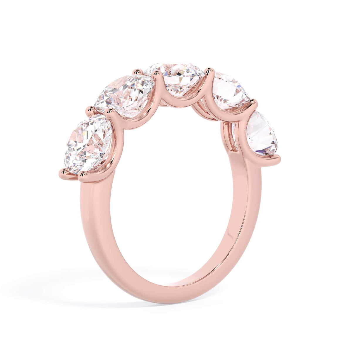 A picture of a five stone diamond wedding ring with round diamonds that are u prong set in rose gold on a white background with a slightly angled, through the finger view.
