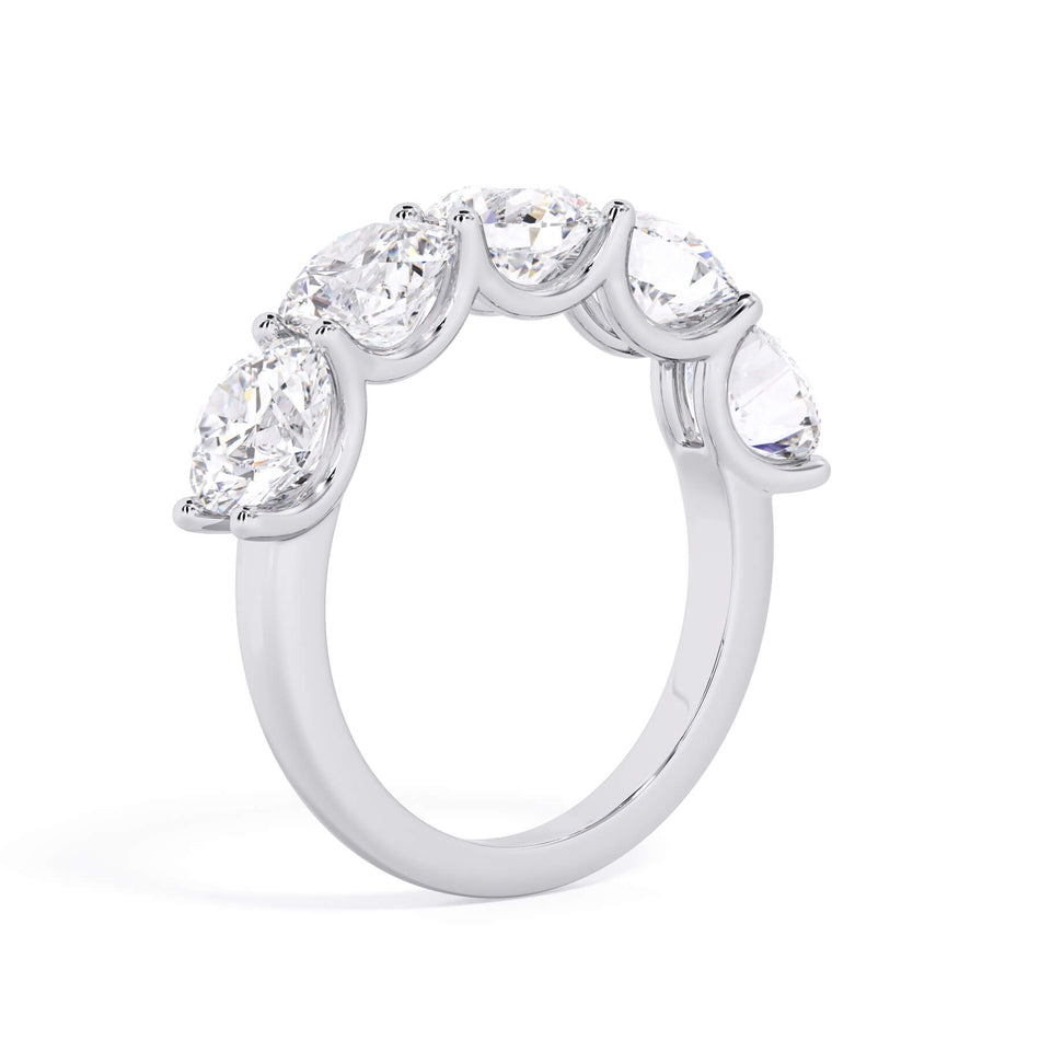 A picture of a five stone diamond wedding ring with round diamonds that are u prong set in white gold or platinum on a white background with a slightly angled, through the finger view.