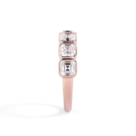 A picture of a seven stone diamond wedding ring with asscher cut diamonds that are bezel set in rose gold on a white background with a side profile view.
