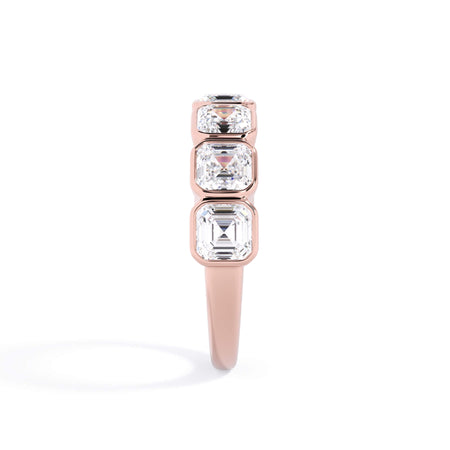 A picture of a seven stone diamond wedding ring with asscher cut diamonds that are bezel set in rose gold on a white background with a side profile view.