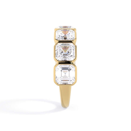 A picture of a seven stone diamond wedding ring with asscher cut diamonds that are bezel set in yellow gold on a white background with a side profile view.