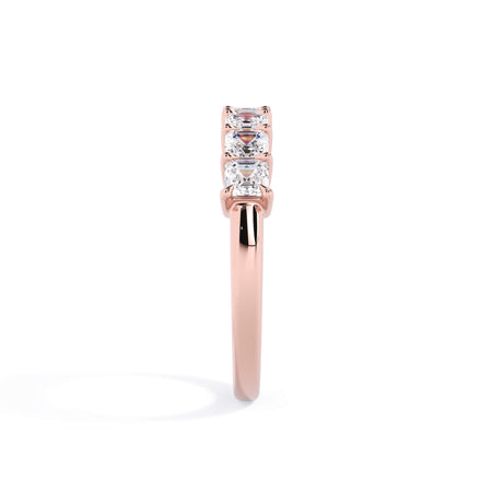 A picture of a seven stone diamond wedding ring with asscher cut diamonds that are shared prong set in rose gold on a white background with a side profile view.
