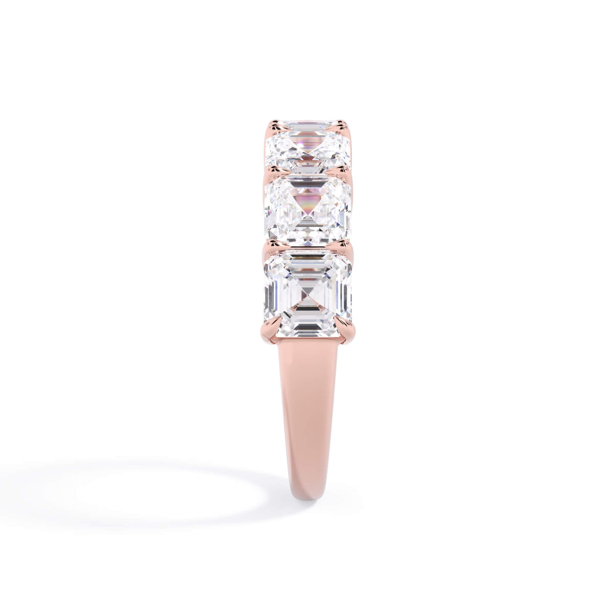 A picture of a seven stone diamond wedding ring with asscher cut diamonds that are shared prong set in rose gold on a white background with a side profile view.