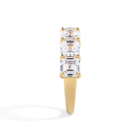 A picture of a seven stone diamond wedding ring with asscher cut diamonds that are shared prong set in yellow gold on a white background with the ring facing forward, lying down.