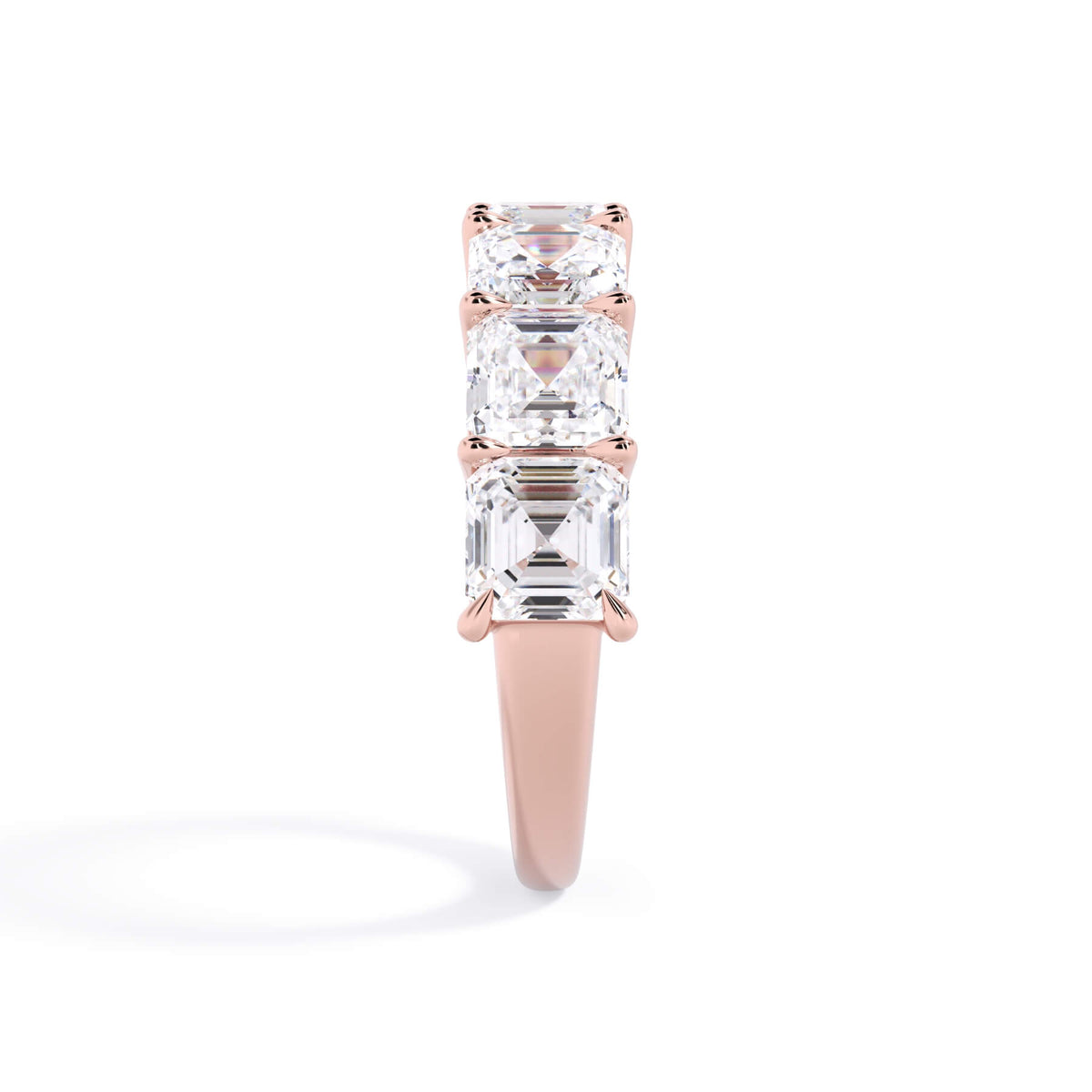 A picture of a seven stone diamond wedding ring with asscher cut diamonds that are shared prong set in rose gold on a white background with a side profile view.